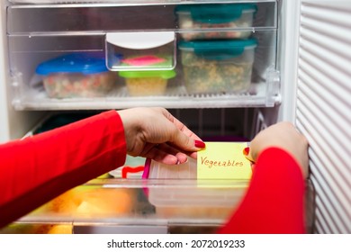 Woman Placing Container With Frozen Mixed Vegetables In Freezer.