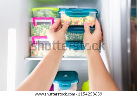 Woman placing container with frozen mixed vegetables in refrigerator.