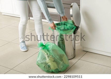 Woman placing garbage bag into empty trash bin in kitchen