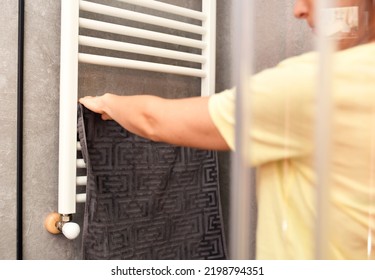 Woman Placing Towel To Dry On Bathroom Radiator In Winter Or Fall.