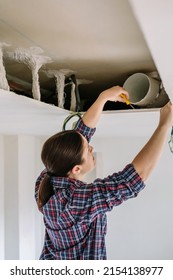 Woman Placing Tube For Kitchen Hood Installation On Kitchen Ceiling