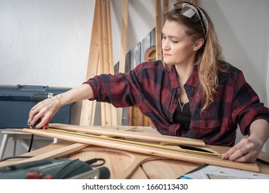 A woman in a plaid shirt in a carpenter's shop. Girl measures the Board with a tape measure. The woman thinks over the concept of a new joinery. Own joinery project. - Powered by Shutterstock