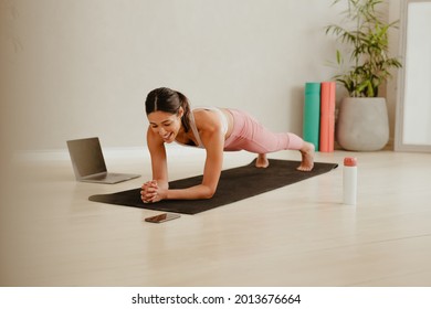 Woman In Plank Position Looking At Her Mobile Phone On Floor. Woman Doing Pilates Workout At Home Watching Video On Mobile Phone.