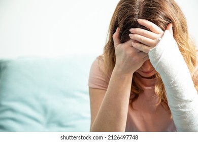 A Woman With A Plaster Cast On Her Arm Holds Her Head.