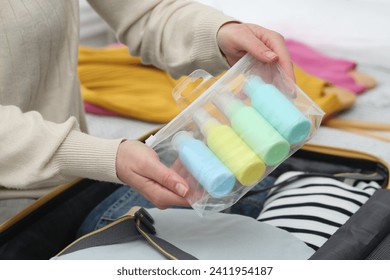 Woman with plastic bag of cosmetic travel kit packing suitcase, closeup. Bath accessories - Powered by Shutterstock