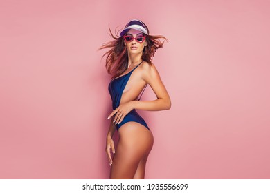 Woman in plastic cap visor and swimwear on pink