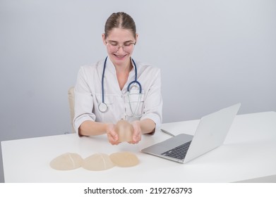 Woman Plastic Surgeon Demonstrating Breast Implants At Her Desk. 