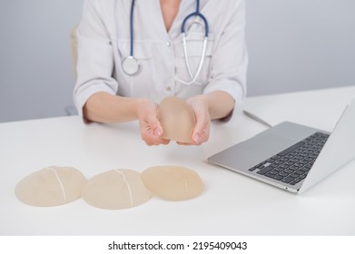 Woman Plastic Surgeon Demonstrating Breast Implants At Her Desk. 