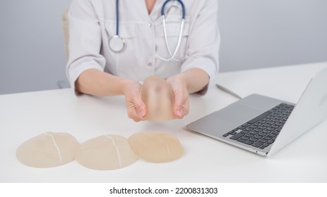 Woman Plastic Surgeon Demonstrating Breast Implants At Her Desk. 