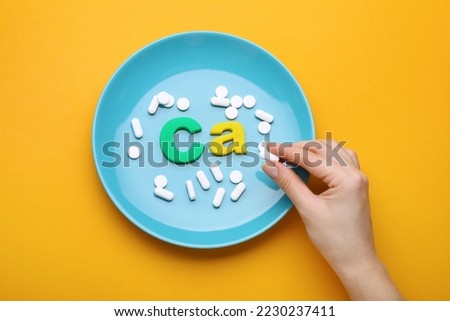 Woman, plate with pills and calcium symbol made of colorful letters on orange background, top view