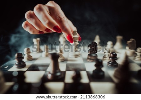 Woman player playing board intelligence game - wooden chess. Female arm with red nails moves piece king, her move. Henpecked, manipulation, psychology, pressure and power concept.