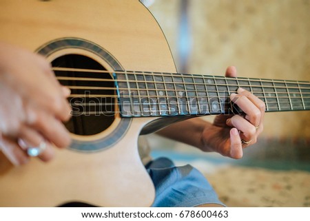 A woman playing acoustic guitar on the bedroom. 