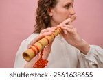 Woman playing bamboo flute with red decorative knot. Close-up portrait on pink background. Musical performance and cultural tradition concept.