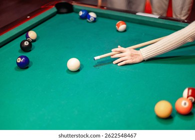 Mujer jugando al billar apuntando la bola blanca con el taco en una mesa de billar verde durante un juego