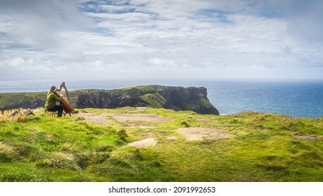 Woman playing harp on the top of the cliff with stunning view on iconic Cliffs of Moher, popular tourist attraction, Wild Atlantic Way, Clare, Ireland - Powered by Shutterstock