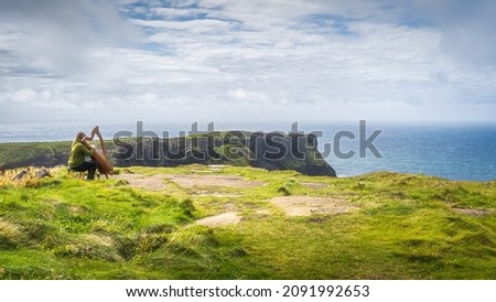 Woman playing harp on the top of the cliff with stunning view on iconic Cliffs of Moher, popular tourist attraction, Wild Atlantic Way, Clare, Ireland