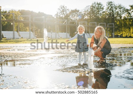 Woman playing with her little daughter in fountain. Little girl having fun with mother outdoors.