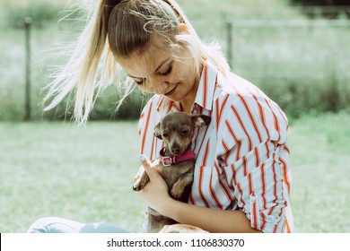 Woman Playing With Little Pinscher Ratter Prazsky Krysarik Crossbreed Hugging Small Dog Outside On Grass During Summer Spring Weather