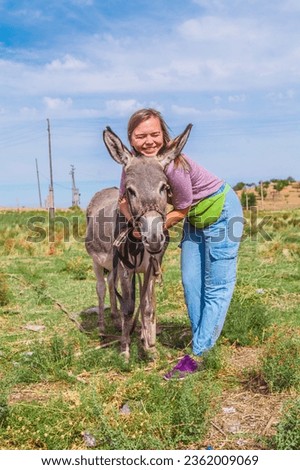 Woman playing natural donkey farm animals.Woman hugging donkey in a funny friendly way. Comical photo. Autumn field.