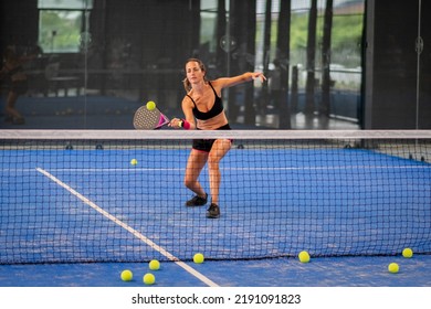 Woman playing padel in a blue grass padel court indoor - Young sporty woman padel player hitting ball with a racket - Shutterstock ID 2191091823