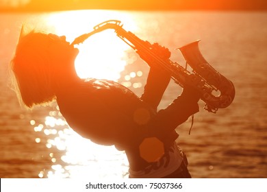 Woman Playing Saxophone Sax At Sunset Beach.