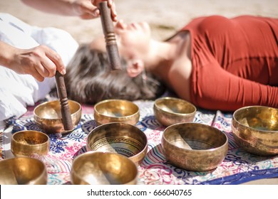 Woman playing a singing bowls also known as Tibetan Singing Bowls, Himalayan bowls. Making sound massage at beautiful sunny day.