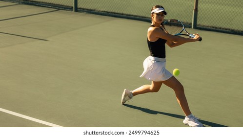 Woman playing tennis, showcasing a backhand shot with racket and ball on the court during a sunny holiday.