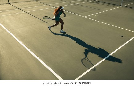 Woman playing tennis at sunset, swinging her racket and casting a long shadow on the court - Powered by Shutterstock