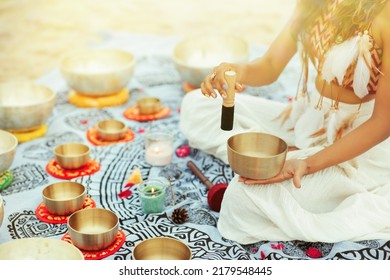 Woman playing Tibetan Singing Bowls with Mallet on Beach. Relaxing Meditative Music Therapy and Sound Healing Massage. Spiritual Yoga Meditation Practice over Sunshine Background