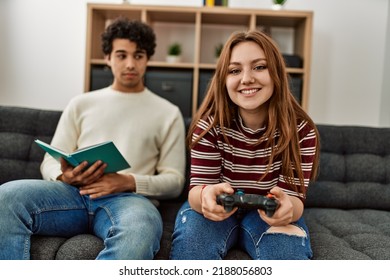 Woman Playing Video Game While Unhappy Boyfriend Read Book At Home.