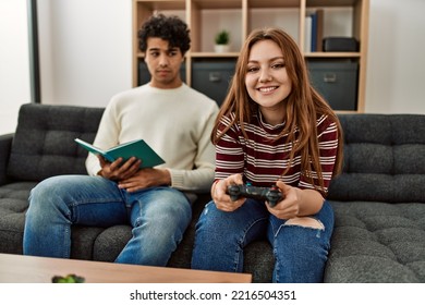 Woman Playing Video Game While Unhappy Boyfriend Read Book At Home.