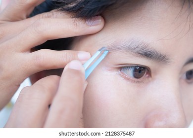 Woman plucking eyebrows with tweezers close up. authentic brown eyes black hair and skin tan asian Thailand. beauty cosmetic concept. - Shutterstock ID 2128375487
