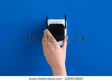 Woman plugging black WiFi repeater in electric socket on blue wall