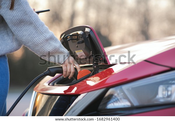 Woman is plugging electric vehicle for charging\
car battery at parking. Close up. Plugged charging cable electric\
vehicle, EV parking, power charger cable, charging port station,\
sustainable future