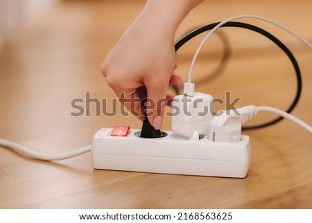 Woman pluging the black wire into white extension cord. Close up of female hand put cabel. Charger