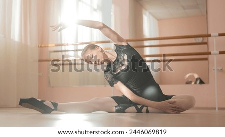 Woman in pointe shoes sits on the floor and does ballet warm-up. 