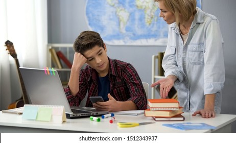 Woman pointing at books scolding son holding smartphone, teen age behavior