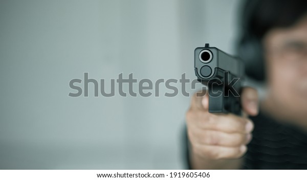 Woman pointing a\
gun at the target. Close-up image of the muzzle of a gun on dark\
background, vintage color\
tone.