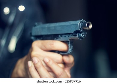 Woman pointing a gun at the target on dark background, selective focus on front gun