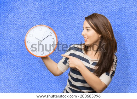 Woman pointing with her finger to a clock. Over blue background