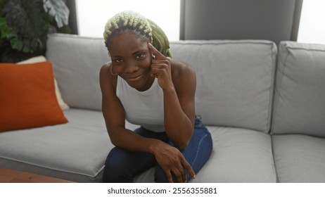 Woman pointing at her head sitting on a sofa in a cozy living room, showing a thoughtful expression with braided hair, conveying a sense of reflection at home. - Powered by Shutterstock