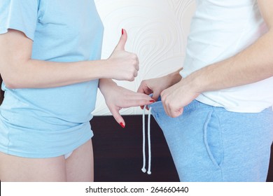 Woman pointing thumb up in direction of male genitalia while man holds open underwear and showing his penis. Question of impotence or sexual organ size . Peny and medical or psychological problem