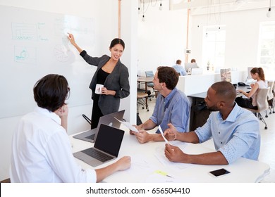 Woman Pointing At Whiteboard At A Meeting In A Busy Office