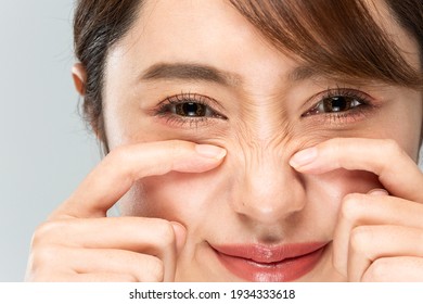A woman is pointing at the wrinkles on her nose. - Shutterstock ID 1934333618