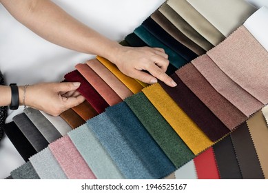 A woman points to a dark burgundy thick fabric, she looks at the catalog of fabrics for making upholstered furniture, she wants to order a new sofa for her living room