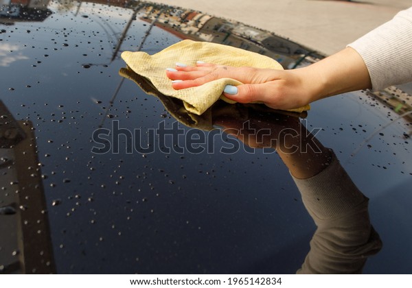 woman polishes the car, uses a\
microfiber cloth and polish to wipe the car\'s body with\
polish.