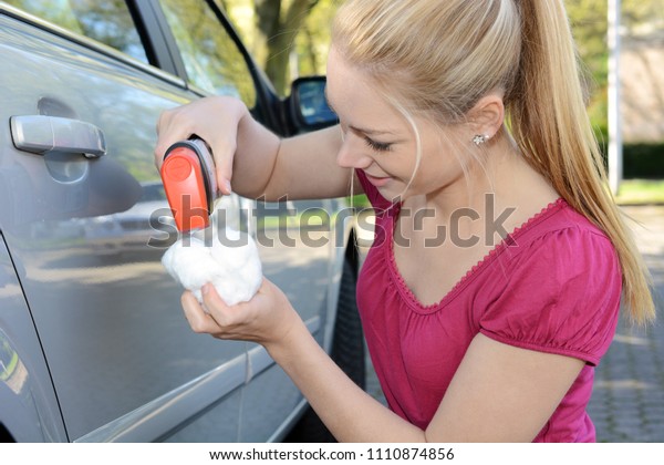 Woman\
polishes her car with polish cotton on a sunny\
day