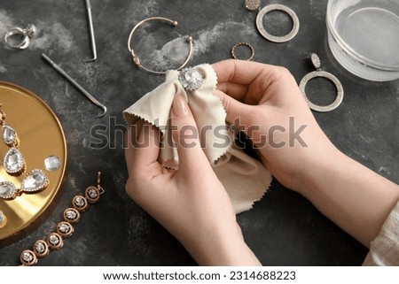 Woman polishing beautiful ring with napkin on grunge background, closeup