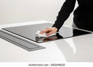 Woman polishing her ceramic induction cooktop built in kitchen appliances with tissue, using special cleaning chemicals to clean glossy white counter, cropped shot