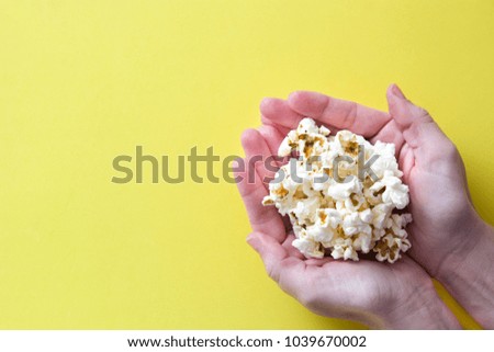 woman with popcorn in hand on yellow background. Copyspace